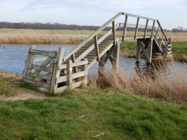 Een brug in een weiland met een rivier