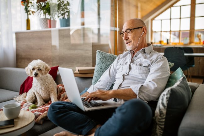 Oudere man met hond op de bank en laptop erbij