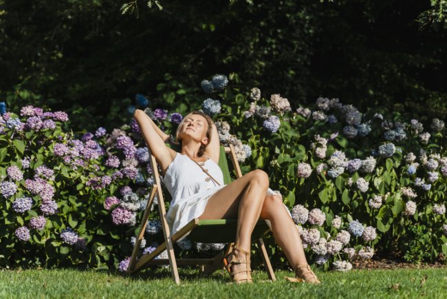Vrouw zit te zonnen tussen hortensias