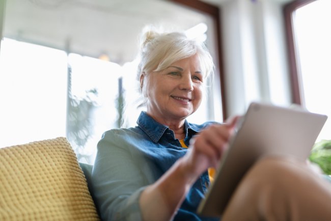 Vrouw zit vrolijk met tablet op de bank te swipen