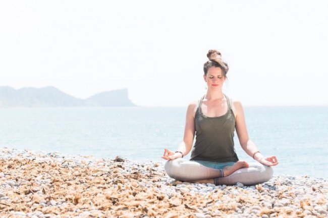 Vrouw zit op het strand een ademhalingsoefening te doen