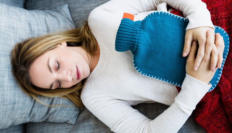 Vrouw ligt op bank met warmwaterkruik op haar buik