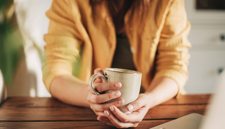 Vrouw zit aan tafel met kop koffie voor zich