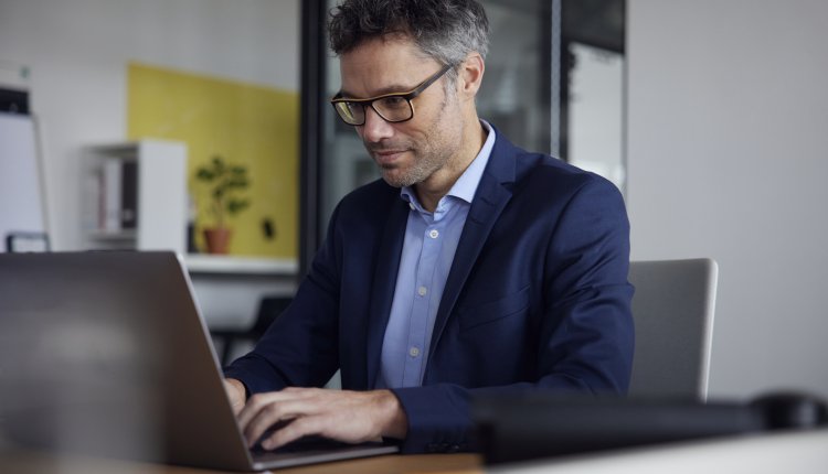Oudere man met bril en colbert is hard aan het werk op zijn laptop