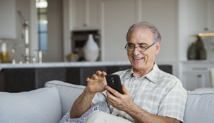 Man is vrolijk met telefoon bezig in huiskamer