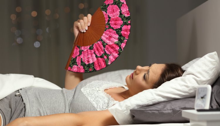 Vrouw ligt met waaier in bed op zoek naar verkoeling