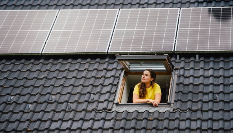 Dak met zonnepanelen, knappe vrouw kijkt uit het raam