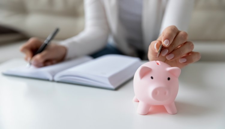 Vrouw schrijft haar uitgaven op en stopt geld in spaarvarken