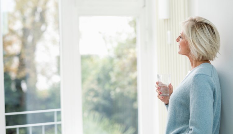 Vrouw drinkt glas water en kijkt naar buiten door het raam
