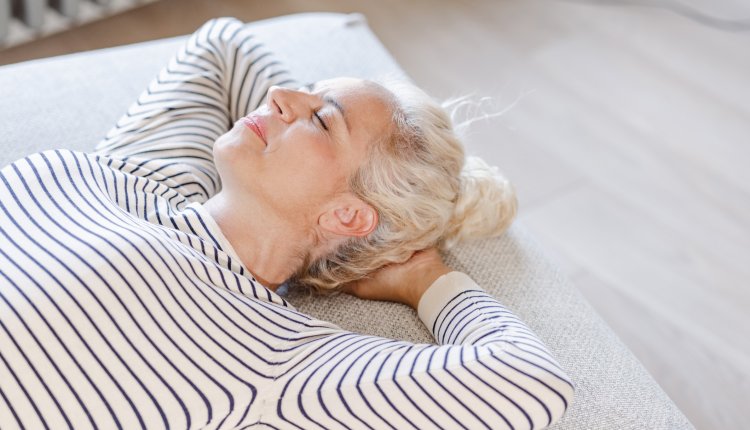 Vrouw ligt op haar rug zonder kussen op haar bed 