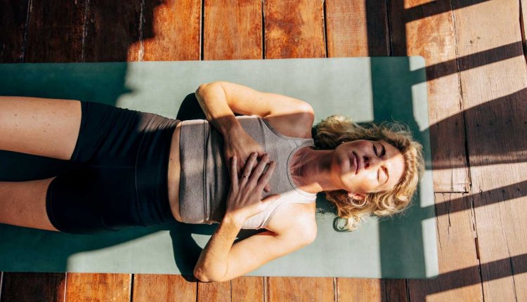 vrouw doet ademhalingsoefeningen op yogamat