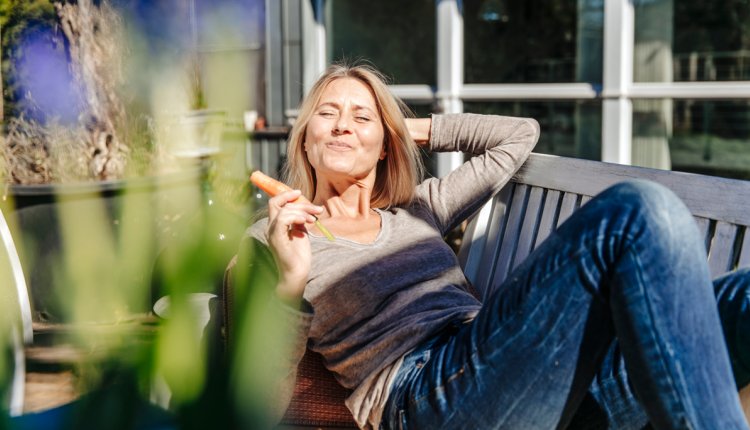 Vrouw zit buiten en eet een wortel
