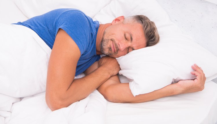 Man ligt op zijn linkerzij te slapen in een bed met wit beddengoed