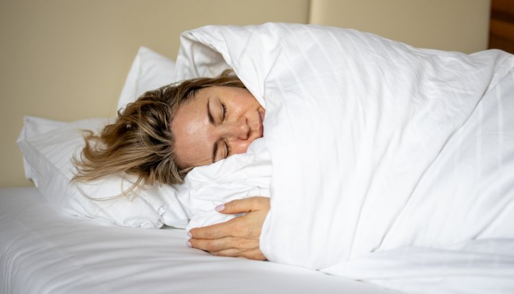 Vrouw ligt in bed op haar zij in wit dekbed