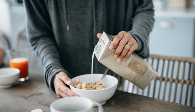 Vrouw schenkt sojamelk over cornflakes