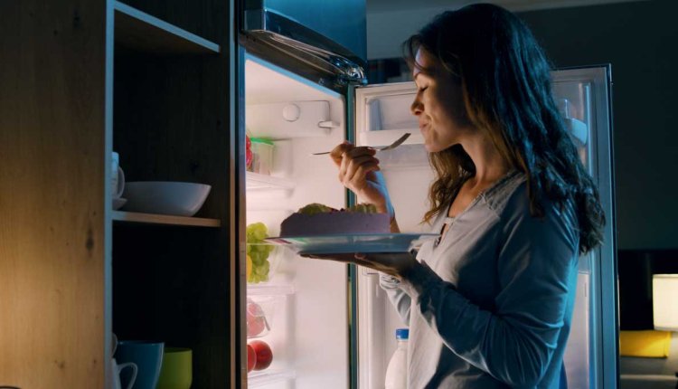 Vrouw eet 's nachts voor de koelkast