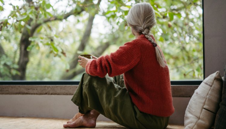 Vrouw zit gehurkt voor het raam naar buiten te staren