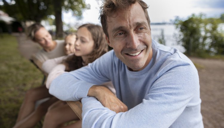Man kijkt weg van camera met familie op achtergrond, weiland met houten palen