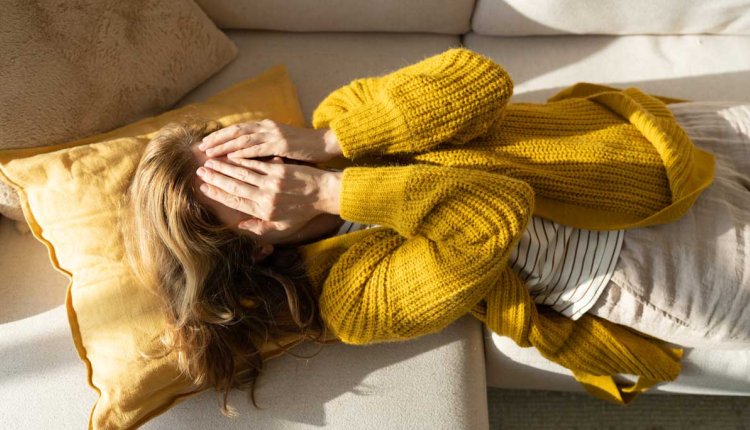 Vrouw met handen voor haar ogen ligt op de bank