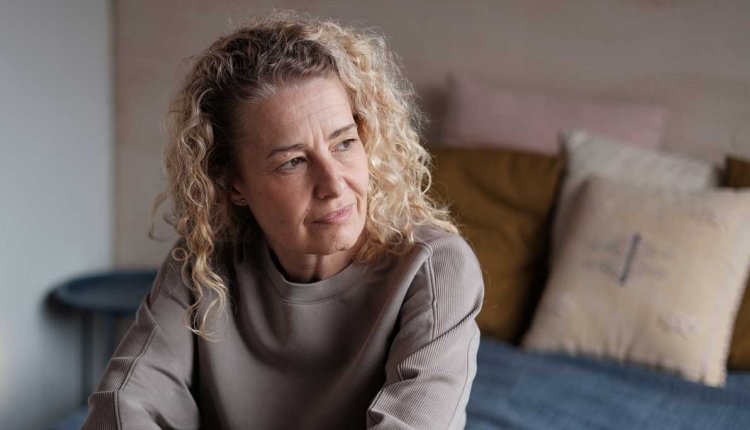 vrouw zit op bed kijkt met zorgelijke blik naar buiten