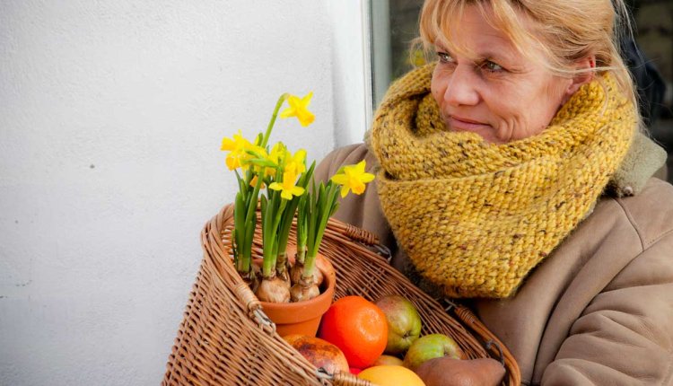 Vrouw met fruit en narcissen in een mand