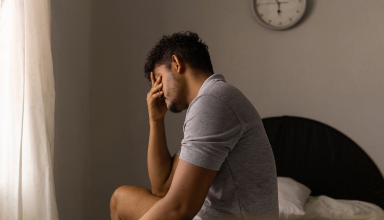 Man zit vermoeid op de rand van zijn bed na een slapeloze nacht