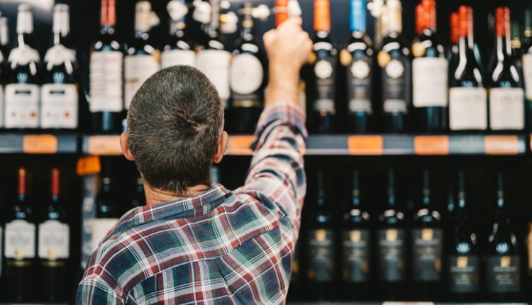 Man pakt een fles wijn uit het rek in de winkel