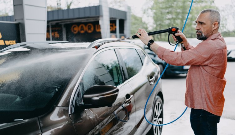 oudere man wast zijn auto bij wasbox