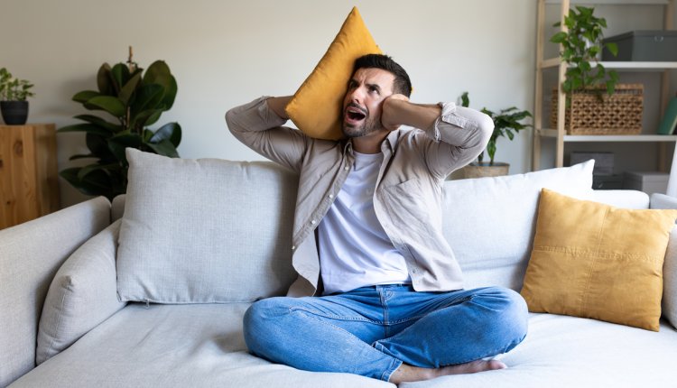 Man met kussen en hand tegen zijn oren, heeft last van herrie van de buren