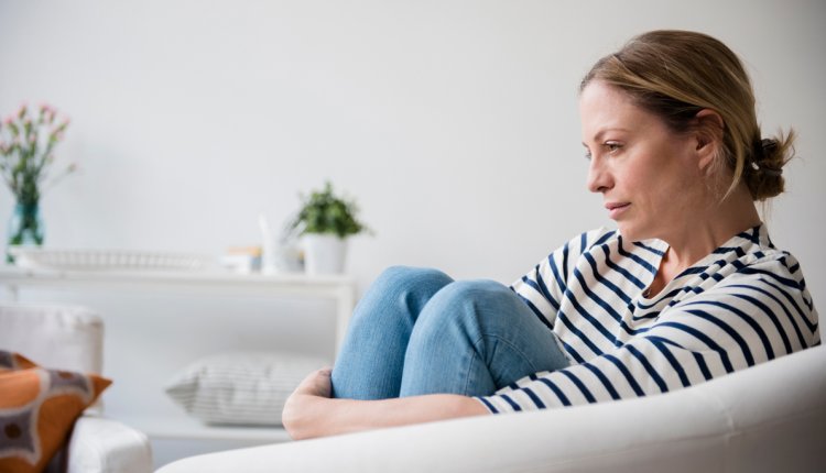 Vrouw zit op de bank thuis staart zorgelijk voor zich uit