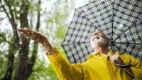 Senior man met baard met gele jas en paraplu voelt of het nog regent in het bos.