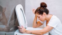 Jonge vrouw hangt over rand van het toilet