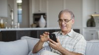 Man is vrolijk met telefoon bezig in huiskamer