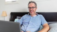 Man zit op de bank blij te spelen met zijn laptop