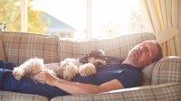 Man slaapt overdag op de bank samen met zijn hondje