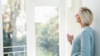 Vrouw drinkt glas water en kijkt naar buiten door het raam