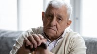Oudere man met wandelstok zit op de bank