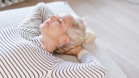 Vrouw ligt op haar rug zonder kussen op haar bed 