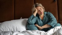 Vrouw zit uitgeput op bed met de handen in het haar