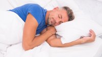 Man ligt op zijn linkerzij te slapen in een bed met wit beddengoed
