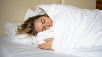 Vrouw ligt in bed op haar zij in wit dekbed