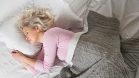 Vrouw ligt heerlijk te slapen in een bed met wit beddengoed met een sprei