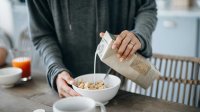 Vrouw schenkt sojamelk over cornflakes