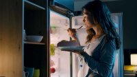 Vrouw eet 's nachts voor de koelkast
