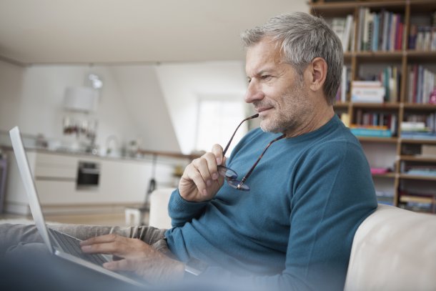 Oudere man checkt email op zijn laptop in de woonkamer met boekenkast
