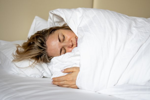 Vrouw ligt in bed op haar zij in wit dekbed