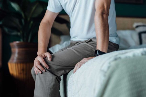 Man met pijnlijke knie zit op bed