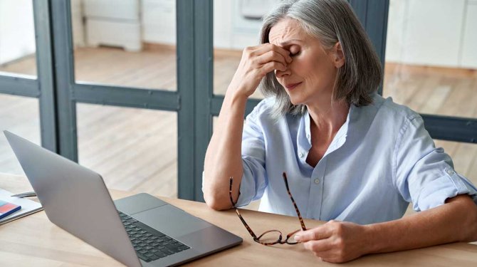 vrouw met vermoeide ogen achter laptop