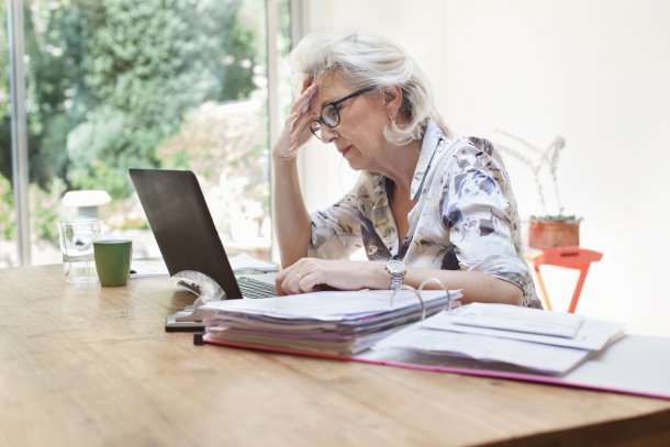 oudere dame aan het werk achter een laptop met veel papierwerk