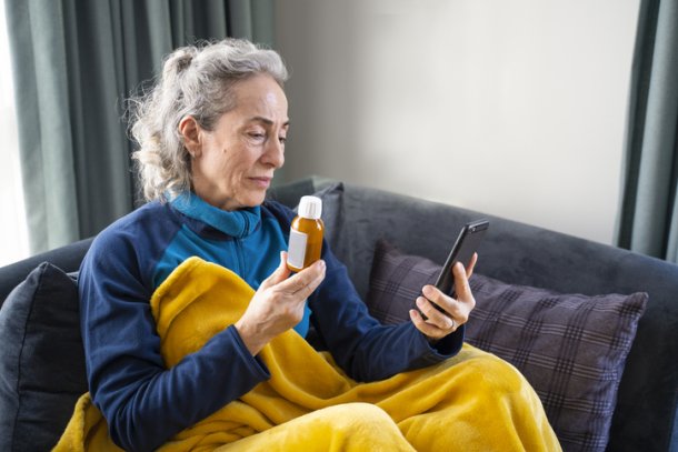 Vrouw zit met smartphone en fles medicatie op de bank